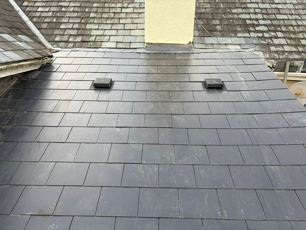 Finished natural slate roof installed by Mets Roofing Southwest on a Devon property — two vents and clean even courses against a yellow-render chimney.